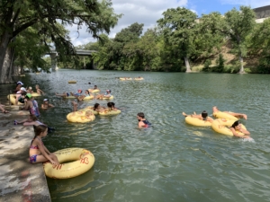 Image of triathletes and their friends and family floating in the Guadalupe River at the finish line festival. Floating is back for the 10th-anniversary celebration.